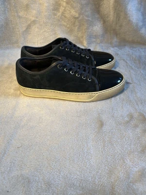 Svarta Lanvin sneakers med lackdetalj - Snygga svarta sneakers från Lanvin med matt mocka och glansig lackdetalj på tån.🙌 Fraktar inom 24h och har ni några frågor så tveka inte på att ställa dem 🙌