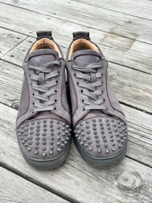 Gråa sneakers med nitar på tån - Unika grå sneakers med matta nitar över hela tån och ovandel i mockaliknande material. Skorna har rundad tå, grå snörning och svart sula. Insidan är beige och designen är riktigt edgy och modern. Jag har inte kvar lådan. Det saknas en nit på ena skon men man får med tre extra nitar. 