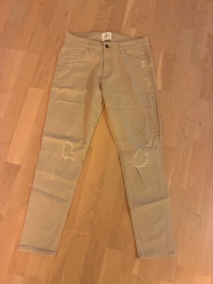 Beige chinos från Vailent Pure - Snygga beige chinos från Vailent Pure med slim fit-passform och slitna detaljer vid knäna. Byxorna har klassiska fickor fram och bak samt knapp och dragkedja i midjan. Perfekta för en avslappnad och trendig stil.