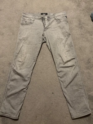 Ljusgrå jeans från Replay - Säljer ett par ljusgrå jeans från Replay. Jeansen har snygga detaljer på bakfickorna och en patch med Replay-loggan bak i midjan. Perfekta för dig som gillar en stilren och avslappnad look.
