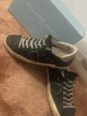 Philippe Model skor - Snygga svarta sneakers från Philippe Model med vita detaljer och gråvita skosnören. Skorna har en klassisk låg siluett och är tillverkade i läder med vit sula och vadderad kant runt hälen. Perfekta för en trendig och avslappnad stil .box ingår skriv till mig får frågor eller mer bilder pris går att diskutera 