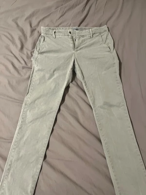 Gråa chinos från Dondup - Snygga gråa chinos från Dondup med klassisk passform och raka ben. Byxorna har fickor fram och bak, bälteshällor och stängs med knapp och dragkedja. Perfekta för dig som gillar stilrena och bekväma byxor i bomull. Ny pris 5000kr