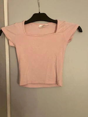 Ljusrosa croppad topp med kort ärm - Söt ljusrosa croppad topp med fyrkantig ringning och korta ärmar. Perfekt till jeans eller kjol för en trendig look. Mjuk och stretchig känsla, troligtvis i bomull eller syntet.