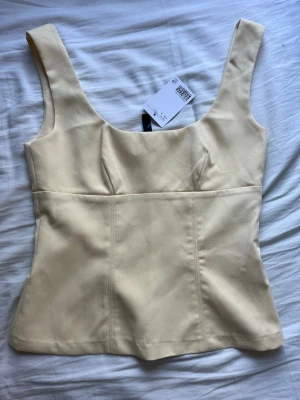 Gul korsettopp från divided på H&M - Stilren gul korsettopp från Divided från H&M med breda axelband och figurnära passform. Toppen har en snygg sömdetalj framtill och är tillverkad i ett slätt material som ger en elegant look. Perfekt att matcha med jeans eller kjol. Jag säljer för att det inte passar mig.