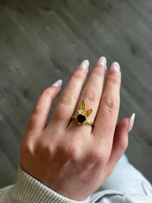 JÄTTE SÖT KANIN RING MED SVART STEN🐰🖤 -  Guldfärgad ring med ett svart hjärta i mitten och en till liten hjärtsten i vit över, och två kanin öron ovanför hjärtat. Ringen är jätte snygg och passar till allt. Den är i helt ny skick och är aldrig andvänd. Jag säljer den bara för att jag fick denna ring i present för att tag sen och jag andvänder inte guld smycken, utan bara silver!🐰🖤