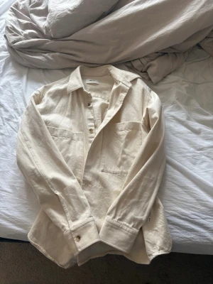 Beige overshirt från NN.07 - Snygg beige overshirt i bomull från NN.07 med klassisk krage, knappar framtill och två bröstfickor. Overshirten har lång ärm och en loose passform som ger en avslappnad vibe. Perfekt för lager på lager under vår och höst.