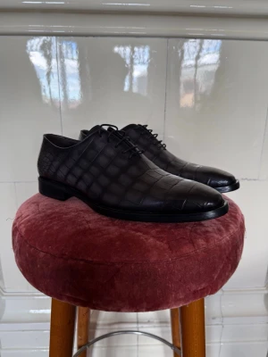 Berluti Miro Soft croc-embossed skor - Berluti Miro Soft croc-embossed skor – helt nya med allt original  * Märke: Berluti * Modell: Miro Soft * Storlek: 42 EU 8 UK * Skick: Helt nya, aldrig använda * Material: Fin kalvskinn (Venezia leather) med croc-mönster * Färg: Svart / mörkgrå med lite brun ton  Ingår:  * Originalbox * Dustbags * Skohorn * Allt original (full set)  Nypris ca 18 000–25 000 kr  Lyxiga skor från Berluti (Paris, 1895), kända för sjukt bra läder och finish. Perfekta till kostym eller dressat.