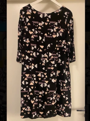 Fin klänning med trekvartsärm - Svart klänning med abstrakt mönster i vitt, beige. Modellen har rund halsringning och trekvartsärm. Klänningen har en rak passform och är tillverkad i ett mjukt, lätt material som ger ett avslappnat intryck.