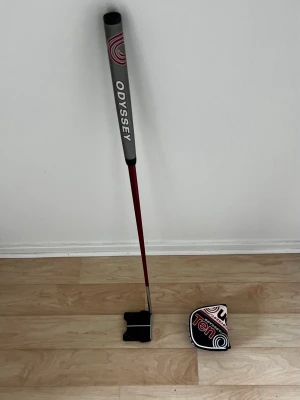 Odyssey Ten golfputter med skydd - Golfputter från Odyssey, modell Ten, med svart och silverfärgad klubbhuvud och röd skaft. Greppet är grått med vit och röd logotyp. Medföljer ett matchande putterskydd med Ten-design. Perfekt för dig som vill ha precision på greenen. 82 cm lång