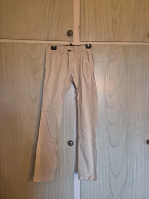 Beige chinos - Säljer ett par klassiska beige chinos  med raka ben och snygga detaljer som bruna knappar och fickor både fram och bak. Materialet är mjukt och skönt bomullstyg som passar perfekt till en avslappnad stil.    Alla kläder rollas innan dom skickas hem då det finns katt i hemmet🐈 Jag stryker och tvättar INTE innan jag skickar det får du stå för själv så det blir som du vill ha det🤗