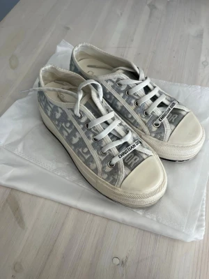 Gråvita sneakers OBS - läs beskrivning! - OBS - förmodligen INTE äkta, köpta secondhand så kvitto finns tyvärr inte. Dustbag medföljer. Beskrivning -  Snygga sneakers i grått och vitt. Skorna har vita snören, gummisula och detaljer med logotypen på plösen. Perfekta för dig som vill ha en lyxig och trendig look. Defekter förekommer (se bilder) Skulle säga att de passar 36! Priset är förhandlingsbart!