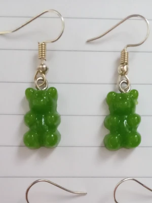 Gröna björn örhängen - Säljer ett par unika örhängen med gröna (inte genomskinliga) gummibjörns-hängen i plast. Örhängena har krokar i metall och är knappt använda. 