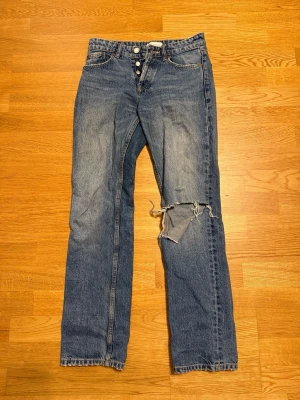 Zara jeans med slitning - Blåa Zara jeans i storlek 34 med hål på vänster knät, midwaist. Säljer pga att dom är för små för mig men passar/lite långa i längden, jag är 156cm. Använda max 10 gånger, finns fler bilder. Säljs inte längre.