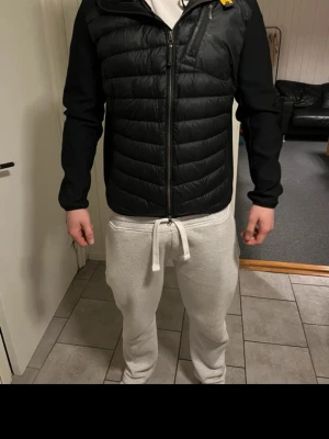 Svart pufferjacka med huva - Säljer en svart pufferjacka med huva och dragkedja framtill. Jackan har quiltad framsida och rygg, samt släta ärmar. Perfekt för kalla dagar och har en sportig look. Detalj i gult vid kragen. Passar dig som gillar stilren och enkel design.