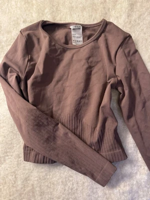 Brun långärmad träningstopp från Stronger - Säljer en brun långärmad topp från Stronger. Tröjan har rund halsringning och ribbade detaljer vid midjan och ärmsluten. Tillverkad i mjukt bomullsmaterial, perfekt för en stilren och enkel look.