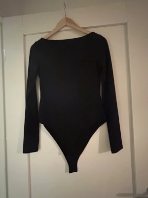 Svart långärmad body - En stilren svart body med långa ärmar och rund halsringning. Tight passform och klassisk design som passar till många olika outfits. Materialet ser ut att vara stretchigt och mjukt, perfekt för lager-på-lager. Inga synliga detaljer eller mönster.Aldrig använd 