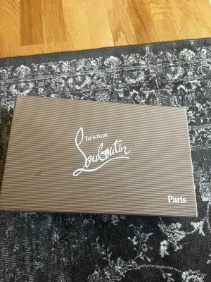 Christian Louboutin - Brunrandig originalkartong från Christian Louboutin med vit logga och tillhörande certifikat och papper. Perfekt för dig som vill ha en snygg och äkta förvaringslåda till dina Louboutin-skor eller accessoarer. PRIS KAN DISKUTERAS!