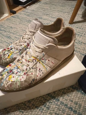Maison Margiela vita sneakers med färgstänk - Maison Margiela paint splatters, bra skick men lite smutsiga, går säkert att få bort. Storlek 42.5 men passar 43(jag har 43, sitter bra på mig). Jätteskön sko men är desperat för pengar just nu. Pris kan definitivt diskuteras vid snabb affär. Hör av dig vid fundering. Mvh Ludwig