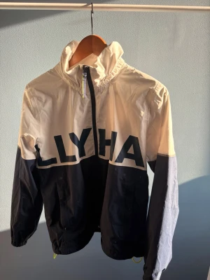 Beige och marinblå vindjacka - Snygg vindjacka i vit och marinblått med stor text över bröst och rygg. Jackan har hög krage, dragkedja framtill och elastiska muddar. Tillverkad i lätt och tåligt material, perfekt för blåsiga dagar. Oversized streetwear-vibe. Perfekt nu till våren🙌🏼