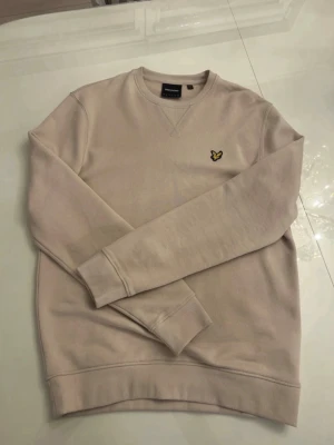 Beige sweatshirt från Lyle & Scott - Pris kan diskuteras  - Snygg beige tröja från Lyle & Scott med klassisk rund halsringning och ribbade muddar. Tröjan har det ikoniska gula fågel-logotypen broderad på bröstet. Perfekt för en stilren och avslappnad look. Ingen prislapp dock aldrig buren!!