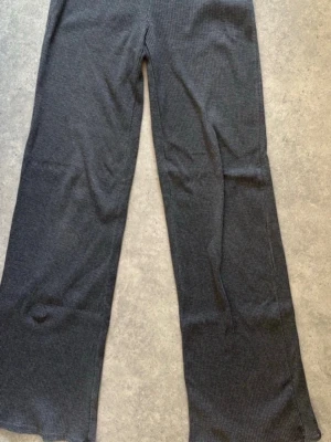 Ribbstickade grå leggings Bershka - Säljer ett par ribbstickade leggings från Bershka i mörkgrå färg. De har hög midja och raka, vida ben. Materialet är mjukt och stretchigt, perfekt för en avslappnad och trendig look.