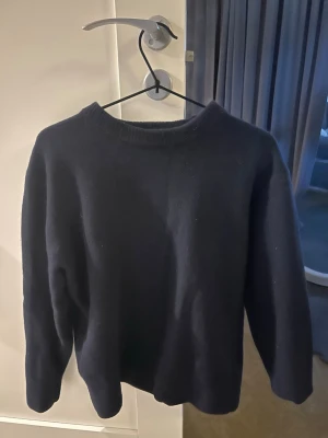 Mörkblå stickad tröja - En enkel och stilren mörkblå stickad tröja med rund halsringning och långa ärmar. Perfekt för lager-på-lager och passar till det mesta. Tröjan har en klassisk passform och ribbstickade muddar vid halsen.