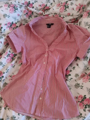 Röd- och vitrandig blus från H&M - Snygg blus/ skjorta från H&M med röda och vita smala ränder, korta ärmar och knappar framtill. ❤️Perfekt för sommaren!❤️ 50 kr + frakt