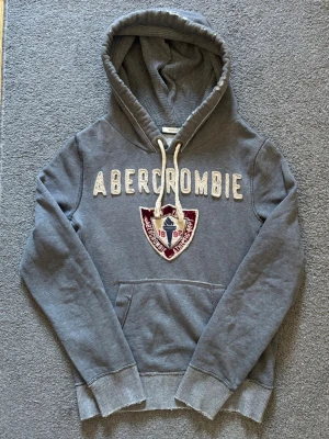 Vintage Abercrombie & Fitch Hoodie - Säljer denna as snygga Abercrombie & Fitch Hoodien | Mycket bra skick, litet hål/skav på baksidan (sista bild)  | Storlek S | Längd ≈ 67cm, Bredd armhåla-armhåla ≈ 57cm | Modell 175cm, 68kg | Hör av vid funderingar! 
