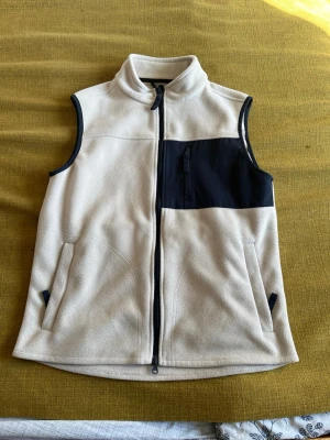 Beige fleeceväst med svarta detaljer - Snygg beige fleeceväst från A Day's March med svarta detaljer och dragkedja framtill. Västen har två sidofickor och en bröstficka med dragkedja i svart tyg. Perfekt för lager-på-lager och chill stil.
