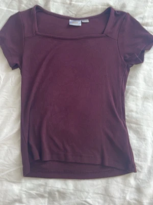 Vinröd topp med fyrkantig ringning - En enkel och stilren vinröd topp med korta ärmar och fyrkantig ringning. Tillverkad i mjukt material som känns skönt mot huden. Perfekt att matcha med jeans eller kjol för en clean look.