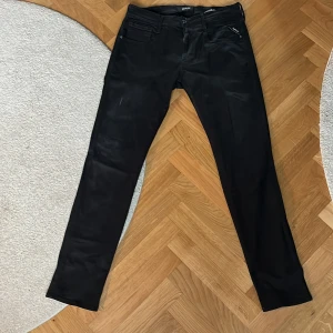 Svarta Replay Hyperflex jeans - Säljer ett par svarta Replay Hyperflex jeans med klassisk femficksdesign och dragkedja. Jeansen har en slim passform och är tillverkade i ett stretchigt material som ger extra komfort. Perfekta för dig som gillar stilrena och bekväma byxor.