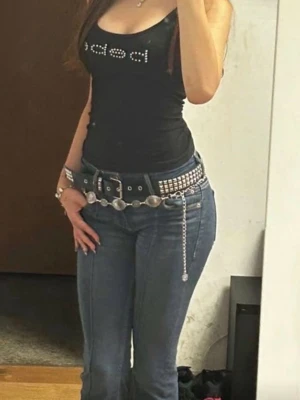 Svart linne från Bebe med strass - Svart figurnära linne från Bebe med tunna axelband och glittrande strassdetaljer som bildar loggan framtill. Perfekt för dig som gillar en enkel men ändå snygg look. Mjukt material och stretchig passform.