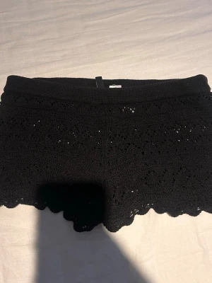 Svarta virkade shorts med spetskant - Svarta shorts med virkad look och snygg spetskant nertill. De har elastisk midja och är perfekta för varma dagar. Ger en chill och trendig vibe till din outfit.