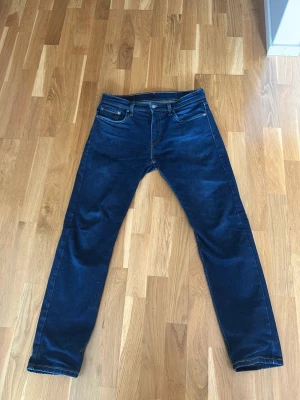 Mörkblå Levi's jeans straight fit - Säljer ett par mörkblå jeans från Levi's med klassisk straight fit och femficksdesign. Jeansen har snygga kontrastsömmar och en ikonisk Levi's patch på bakfickan. Materialet är slitstark denim som känns bekvämt och håller formen. Mycket bra skick.