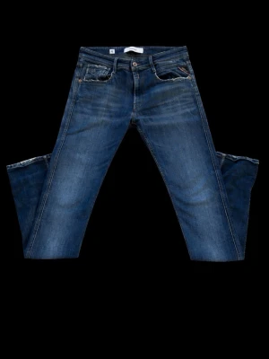 Blå slim fit jeans med slitningar - Snygga blå slim fit jeans med lätt slitna detaljer och klassisk femficksdesign. Jeansen har en något tvättad look och raka ben. Perfekta för en avslappnad och trendig stil. Materialet är troligtvis bomull med stretch för extra komfort.