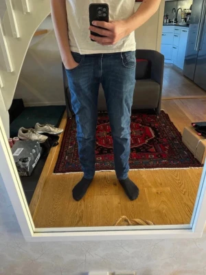 Replay jeans - anbass - Säljer ett par blå slim fit jeans med vita kontrastsömmar och klassisk femficksdesign. Jeansen har normal midja och är tillverkade i ett mjukt denimtyg som sitter snyggt längs benen. Perfekta för dig som gillar en enkel och stilren look. Jeansen är i storlek 32W 34L. Hör av er vid funderingar!