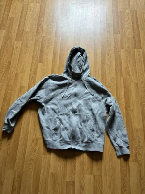 Grå hoodie från Nike med logga - Säljer en klassisk grå hoodie från Nike med broderad vit logga på bröstet. Hoodien har huva med dragsko och en stor magficka framtill. Tillverkad i mjukt bomullsmaterial och har ribbade muddar vid ärmar och nederkant. Perfekt för en avslappnad och sportig stil.
