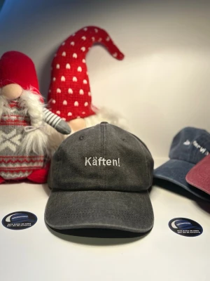 Keps ”Käften” svart - Säljer en svart keps i tvättad bomull med böjd skärm och broderad texten 'Käften!' framtill. Klassisk sexpanelsdesign med justerbar rem bak. Perfekt för dig som vill ha en keps med attityd och enkel stil.
