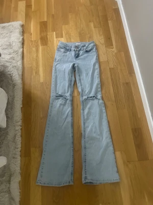Ljusblå bootcut jeans med slitningar - Säljer ett par ljusblå bootcut jeans med slitningar. Jeansen är low waist och klassisk femficksdesign. Perfekta för en avslappnad och trendig look. Kan tänka mig diskutera pris.