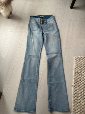 Ljusblå bootcut jeans med fickor från madlady - Säljer ett par ljusblå bootcut jeans med stora framfickor och markerade sömmar. Jeansen har hög midja och utsvängda ben, vilket ger en retro och trendig look. Perfekta för dig som gillar en avslappnad men ändå stilsäker stil.Jag är cirka 172 cm men kan också sys upp. 