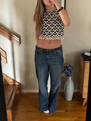 Croppad virkad topp med fransar - Säljer en croppad virkad topp i svart och beige med snyggt mönster och fransar längst ner. Toppen är ärmlös och har en loose passform, perfekt för sommarens alla tillfällen. Supersnygg att styla med jeans eller kjol!