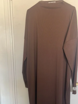 Brun långärmad ribbad klänning - En enkel och stilren brun långklänning från Soft Goat med ribbad struktur. Klänningen har långa ärmar och en rak passform som ger ett avslappnat intryck. Perfekt för dig som gillar minimalistisk design och mjuka material. PRIS GÅR ATT DISKUTERAS! 