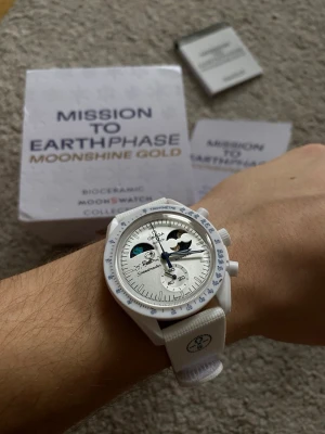 Omega x Swatch MoonSwatch Earthphase Moonshine Gold - Säljer en Omega x Swatch MoonSwatch Mission to Earthphase Moonshine Gold Snoopy Snowflake Edition. Klockan har vit boett och armband, blå visare och detaljerad urtavla med månfasindikator. Biokeramisk konstruktion och cool design som sticker ut på handleden.