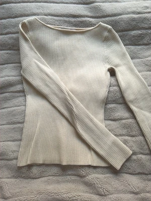 Beige ribbstickad tröja - Säljer en stilren beige ribbstickad tröja med lång ärm och figurnära passform. Tröjan har en bred, rundad halsringning och är tillverkad i ett mjukt, stretchigt material som sitter snyggt på kroppen. Perfekt basplagg för din garderob.