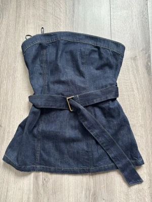 Mörkblå jeans tubtopp med bälte - Snygg mörkblå jeans tubtopp med tillhörande bälte i midjan. Helt ny med prislapp! Köpte den för cirka 500kr. Den är mer som en M! 