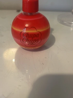 Chupa Chups Cherry Splash parfym - Rolig och färgglad parfym från Chupa Chups i doften Cherry Splash. Flaskan är rund och röd med gula detaljer och har Chupa Chups-loggan på framsidan. Perfekt för dig som gillar söta och fruktiga dofter. Flaskan är tillverkad i plast.