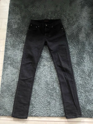 Svarta slim fit jeans från nudie jeans  - Snygga svarta slim fit jeans från nudie med klassisk femficksdesign och raka ben. Jeansen har normal midja och är tillverkade i stretchigt denimtyg för en bekväm passform. Perfekta för dig som gillar en stilren look. Skriv om du har några frågor, pris kan såklart också diskuteras!