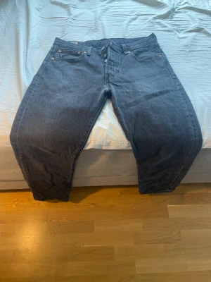 Svarta raka jeans från Levi's - Säljer ett par svarta jeans från Levi's med rak passform och klassisk femficksdesign. Jeansen har knappgylf och är tillverkade i slitstark denim. Perfekta för dig som gillar en tidlös och avslappnad stil.