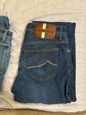 Jacob Cohën jeans  - Snygga blå jeans från Jacob Cohën med klassisk femficksmodell och raka ben. Jeansen har kontrastsömmar och en unik bakficka med vit detaljsöm. Tillverkade i mjukt denimtyg med läderpatch bak i midjan. Modellen är bard och i size 31. De är köpte för 6500 på butiken stenströms i Helsingborg.