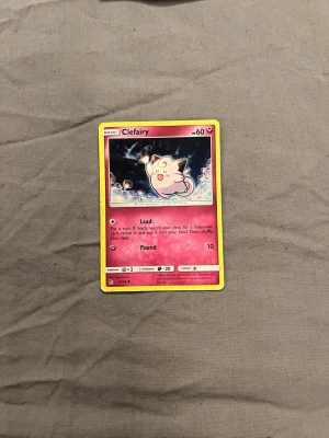 Pokémonkort Clefairy - Pokémonkort med Clefairy-motiv. Kortet har en rosa ram och färgstark illustration av Clefairy i mitten. Tillverkat i laminerad papp med tryckt text och bild. Perfekt för samlare eller dig som gillar Pokémon och trading cards.